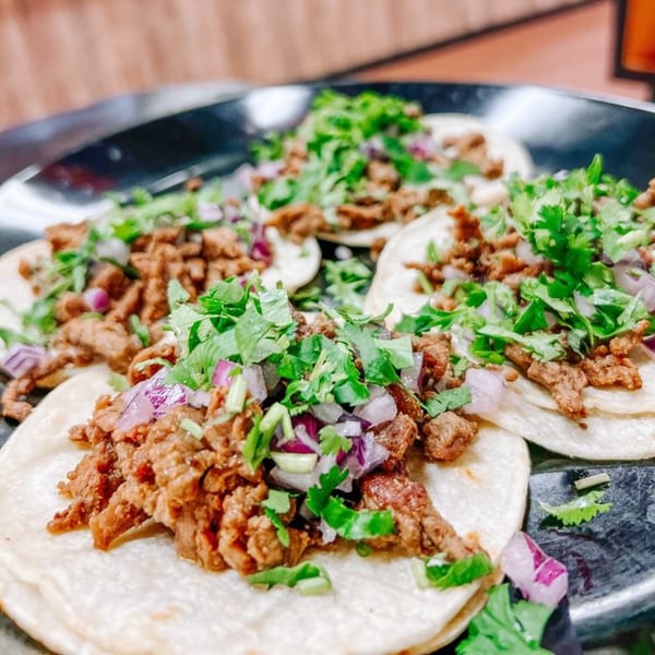 Close-up of four Tacos El Guero #1 street tacos with carne asada, cilantro, and red onion.
