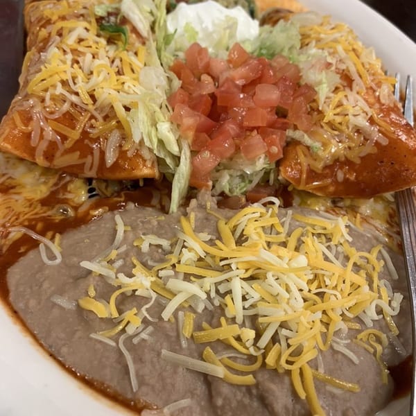 Two enchiladas with red sauce, shredded cheese, lettuce, diced tomatoes, and a side of refried beans.